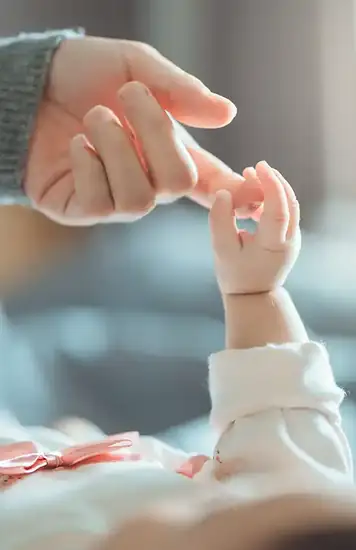 Eine kleine Babyhand greift nach einem erwachsenen Finger.